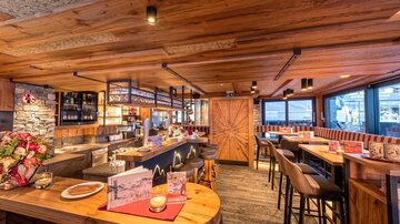 Ein gemütliches Restaurant mit Holzdekor und einer einladenden Bar. Große Fenster bieten einen schönen Blick auf die Umgebung.