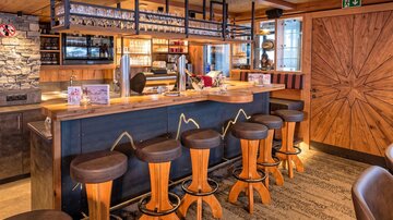 Eine gemütliche Bar mit Holzstühlen und einer einladenden Theke. Der Raum hat eine warme Atmosphäre und ist geschmackvoll eingerichtet.