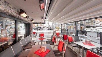 Ein modernes Café mit eleganten Tischen und roten Stühlen. Große Fenster bieten einen Blick auf die Umgebung.