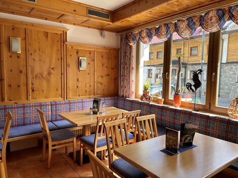 A cozy restaurant with wooden furniture and checkered upholstery.  
Large windows let in plenty of light and offer a view outside.