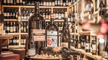 Eine Auswahl an Weinen in einer Weinhandlung. Mehrere große Weinflaschen stehen auf einem Holzfass, umgeben von Weinregalen.