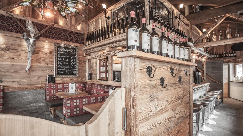 Ein gemütliches Restaurant mit Holzdekor und einer Bar. Die Flaschen stehen auf einem Holzregal, und es gibt Sitzgelegenheiten für Gäste.