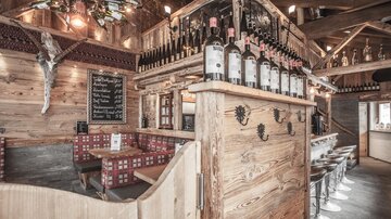 Ein gemütliches Restaurant mit Holzdekor und einer Bar. Die Flaschen stehen auf einem Holzregal, und es gibt Sitzgelegenheiten für Gäste.