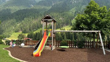 Ein Spielplatz umgeben von schönen Bergen. Die Rutsche ist bunt und es gibt eine Schaukel für Kinder.