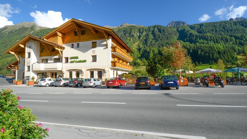 Ein hübsches Hotel mit traditioneller Architektur liegt am Straßenrand. Im Hintergrund sind grüne Berge und Bäume zu sehen.