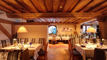 Ein gemütliches Restaurant mit Holzdecke und warmem Licht. Die Tische sind elegant gedeckt und laden zum Verweilen ein.