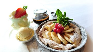 Ein köstlicher Dessertteller mit einem Apfel-Bananen-Auflauf, garniert mit frischen Beeren und Minze. Dazu gibt es Eiscreme und eine süße Sauce.