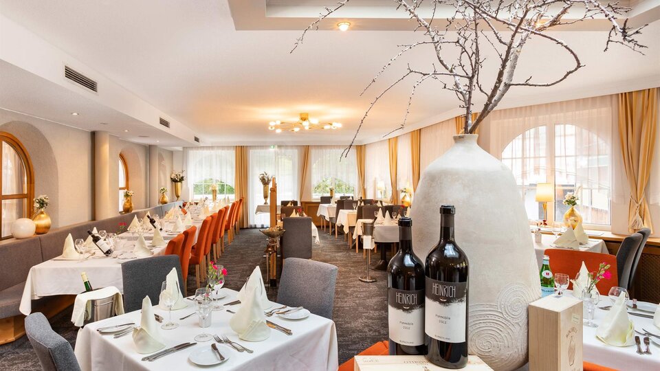 Ein elegantes Restaurant mit gedeckten Tischen und stilvoller Dekoration. Ein großer, dekorativer Krug steht im Vordergrund neben zwei Flaschen Wein.