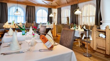 Ein elegant eingerichtetes Restaurant mit holzverkleideten Wänden und gemütlichen Tischen. Die Tische sind mit weißen Tischdecken und dekorativen Servietten gedeckt.