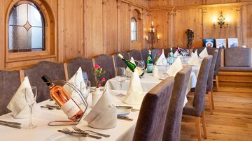 Ein eleganter Speisesaal mit Holzvertäfelung und einer langen Tafel, die für ein festliches Dinner gedeckt ist. Auf der Tafel stehen Weinflaschen und dekorative Servietten.