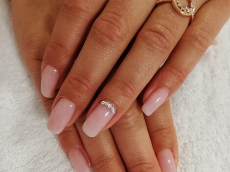 Zwei Hände mit frisch manicurierten, rosa Nägeln liegen auf einem weißen Handtuch. Auf einigen Nägeln sind kleine Schmucksteine.