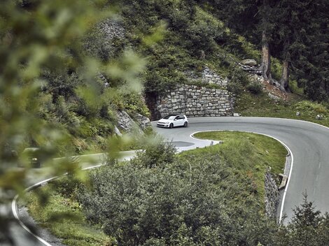 A winding road through a green landscape. A car is driving around a sharp turn.