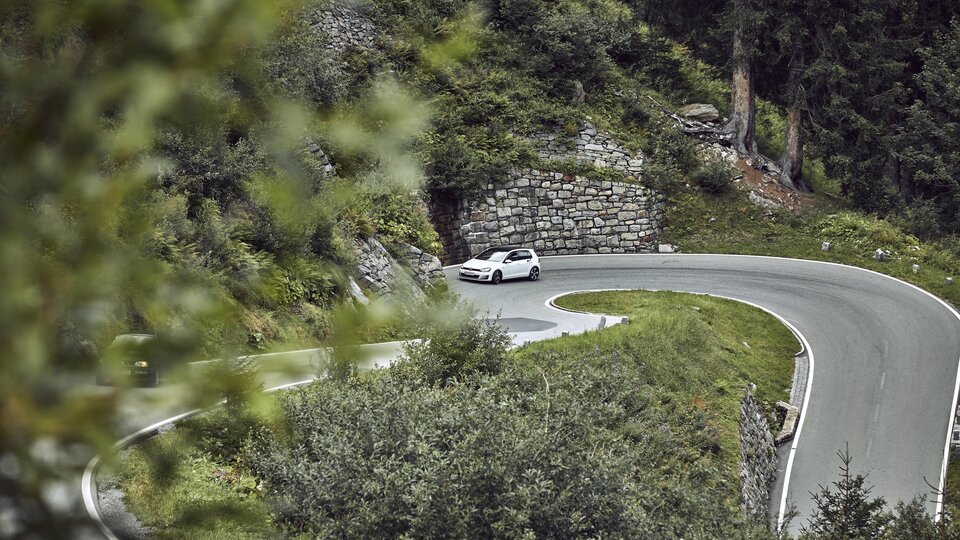 A winding road through a green landscape. A car is driving around a sharp turn.