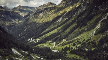 A picturesque mountain landscape with gentle hills and deep valleys. The winding road meanders through the green vegetation.