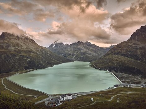 A beautiful mountain lake, surrounded by tall mountains and dramatic clouds. The calm water surface reflects the surrounding landscape.