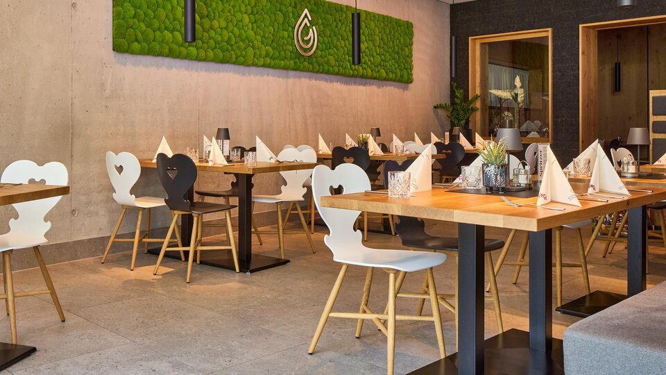 Ein modernes Restaurant mit stilvollen Tischen und Stühlen. An der Wand ist eine lebendige Pflanzenwand zu sehen, die eine einladende Atmosphäre schafft.