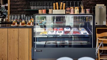 Eine Eistheke in einem modernen Café mit verschiedenen Eissorten. Im Hintergrund stehen Gläser und Waffeln dekoriert auf einem Regal.
