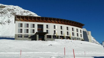 Ein modernes Hotel in den Bergen, umgeben von Schnee. Der klare blaue Himmel sorgt für eine malerische Atmosphäre.