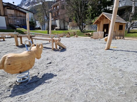 Ein Spielplatz mit einem Holzspringpferd und einem Spielhaus. Der Boden besteht aus Sand und es gibt weitere Spielgeräte in der Nähe.