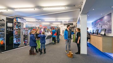 Ein Skiverleih mit Ski und Ausrüstung in einem modernen Geschäft. Einige Kunden, darunter Kinder, sind im Geschäft beschäftigt.