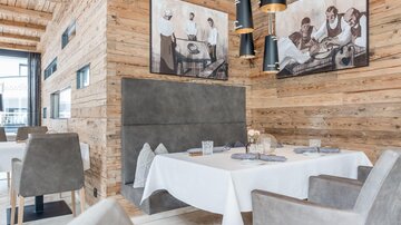 Ein stilvolles Restaurant mit Holzverkleidung und modernen Möbeln. Die Wände sind mit Kunstwerken dekoriert, die historische Szenen zeigen.