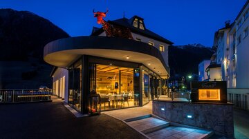 Ein modernes Gebäude mit einer markanten, geschwungenen Fassade und großen Fenstern. Der Außenbereich ist gut beleuchtet und es gibt eine interessante Dekoration an der Fassade.