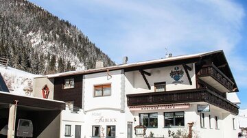 Ein charmantes Gästehaus im Schnee mit einem malerischen Berg im Hintergrund. Die Fassade ist traditionell und einladend.