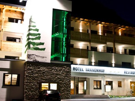 Ein modernes Hotel mit Holzfassade und angenehmer Beleuchtung bei Nacht. Das Hotel Tannenhof bietet eine einladende Atmosphäre und einen Restaurantbereich.
