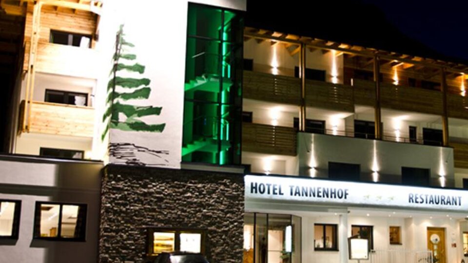 Ein modernes Hotel mit Holzfassade und angenehmer Beleuchtung bei Nacht. Das Hotel Tannenhof bietet eine einladende Atmosphäre und einen Restaurantbereich.