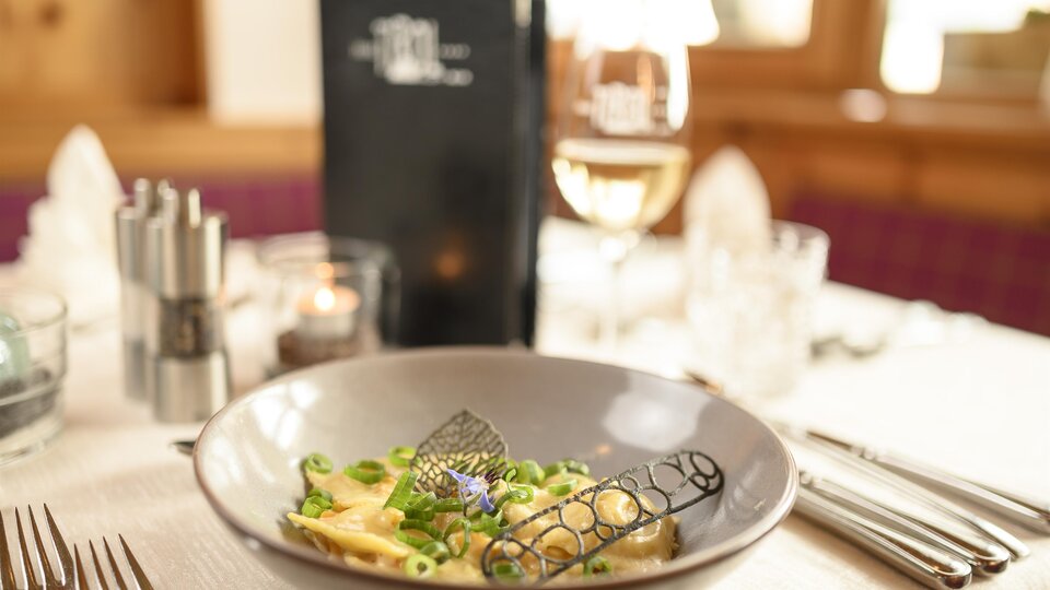 Ein stilvoll gedeckter Tisch mit einem Teller Pasta und frischem Gemüse. Im Hintergrund sind ein Getränk und eine Menükarte zu sehen.