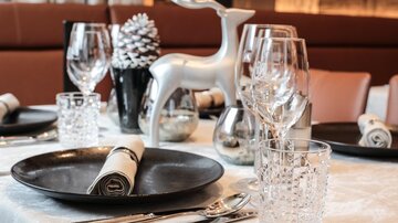 Ein festlich gedeckter Tisch mit eleganten Gläsern und silbernem Deko. Im Mittelpunkt steht ein stilvoller Rentier-Dekorationsartikel.