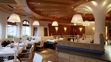 Ein gemütliches Restaurant mit Holzdekor und sanfter Beleuchtung. Es gibt Tischdecken und Blumen auf den Tischen, die eine einladende Atmosphäre schaffen.