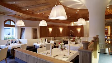 Ein stilvolles Restaurant mit Holzmöbeln und sanfter Beleuchtung. Die Tische sind elegant eingedeckt und laden zum Verweilen ein.