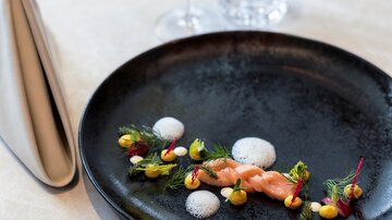 Ein elegant angerichteter Teller mit Garnelen und buntem Gemüse. Ein Glas Wein ergänzt das gehobene Gericht auf dem Tisch.
