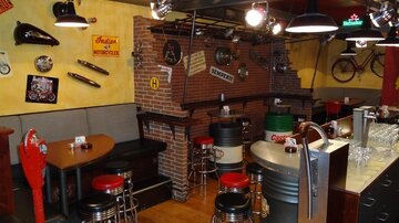 Eine gemütliche Bar mit Sitzgelegenheiten aus Metall und Holz. Die Wände sind mit verschiedenen Motorradzubehörteilen und nostalgischen Dekorationen geschmückt.