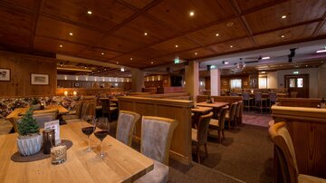 Ein gemütliches Restaurant mit Holzdekor und warmem Licht. Tische sind vorbereitet und es herrscht eine einladende Atmosphäre.