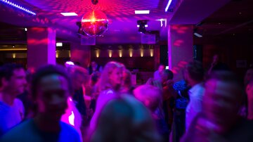Eine lebhafte Disco mit tanzenden Menschen und bunten Lichtern. Ein Discokugel strahlt im Hintergrund und schafft eine feierliche Atmosphäre.