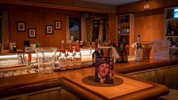 Eine gemütliche Bar mit Holzvertäfelungen und einer Auswahl an Getränken. Auf der Theke steht eine Flasche und ein Porträt eines Mannes.