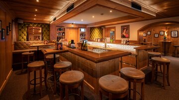 Eine gemütliche Bar mit Holzvertäfelung und warmem Licht. Es gibt Sitzgelegenheiten und eine einladende Atmosphäre.