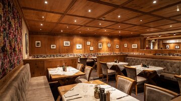 Ein gemütliches Restaurant mit holzverkleideten Wänden und beleuchteten Decken. Die Tische sind ordentlich gedeckt und es gibt eine warme, einladende Atmosphäre.