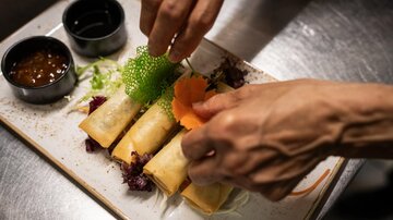 Ein Teller mit Frühlingsrollen wird dekoriert. Dazu gibt es verschiedene Soßen und frisches Gemüse.