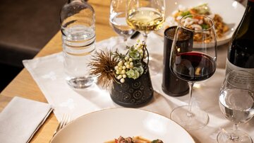 Ein schön angerichteter Tisch mit zwei Tellern Essen, Gläsern mit Wein und Wasser. Im Vordergrund sieht man ein Gericht mit Reis und buntem Gemüse.