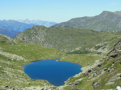 A beautiful mountain lake surrounded by green meadows and mountains. The sky is clear and blue.