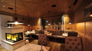 Ein gemütliches Restaurant mit Holzwänden und einer warmen Atmosphäre. Es gibt komfortable Sitzplätze und einen Kamin, der das Ambiente unterstreicht.
