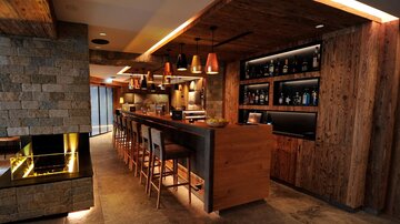 Eine moderne Bar mit Holzverkleidung und stilvollen Lichtakzenten. Die Bar bietet Platz für mehrere Gäste und ist gut sortiert mit Getränken.