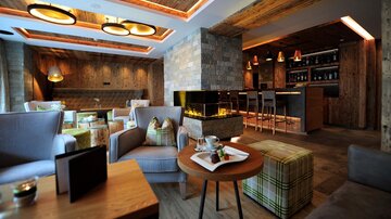 Ein modernes Café mit gemütlichen Sitzgelegenheiten und rustikalem Holzdekor. Im Hintergrund ist eine Bar mit stilvollen Lampen und einem Kamin zu sehen.