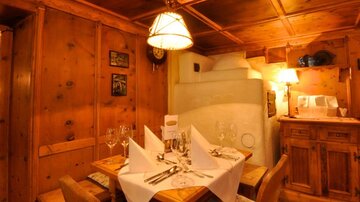 Ein gemütlicher Essbereich mit Holzwänden und einer warmen Beleuchtung. Der Tisch ist elegant gedeckt mit Gläsern und Stoffservietten.