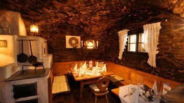 Ein gemütliches Restaurant mit Steinwänden und Holzinterieur. Der Tisch ist rustikal gedeckt und es gibt Kerzenlicht für eine einladende Atmosphäre.