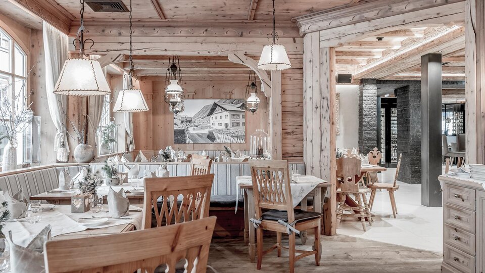 Ein gemütliches Restaurant mit Holzverkleidung und warmem Licht. Es sind Tische mit eleganten Tischdecken und Stühlen aus Holz eingedeckt.