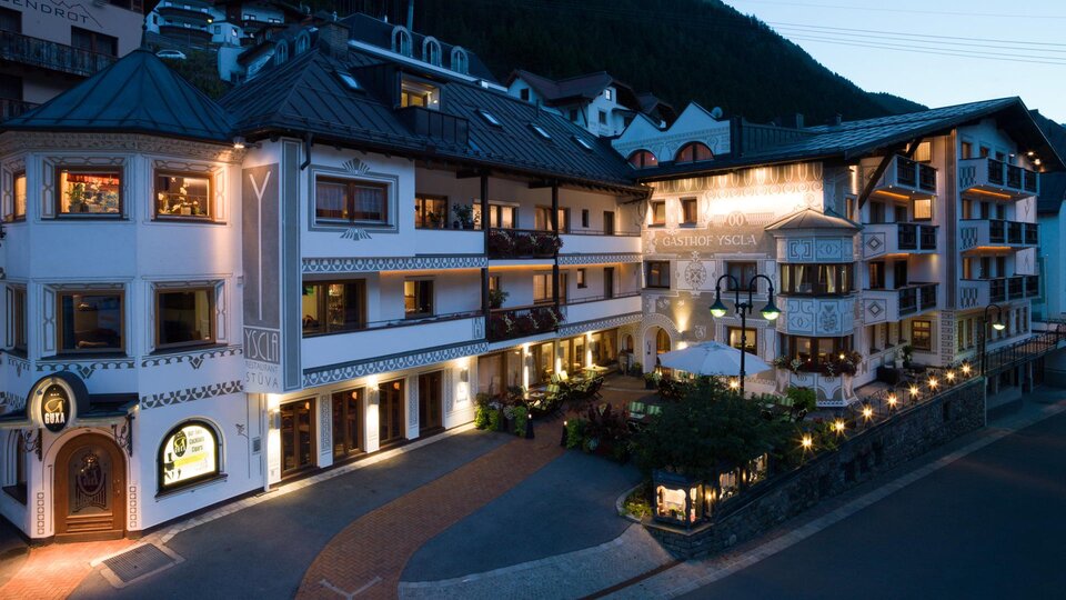 Ein charmantes Gebäude im alpenländischen Stil, beleuchtet in der Abenddämmerung. Umgeben von saftigen Bergen und einer einladenden Atmosphäre.